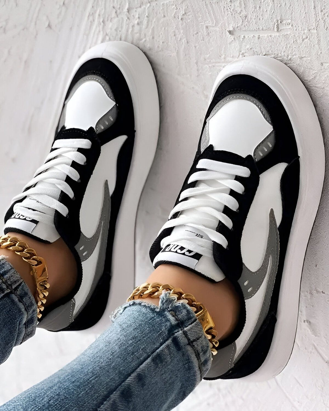 Une paire de baskets blanches, grises et noires avec des lacets blancs sur un fond blanc.