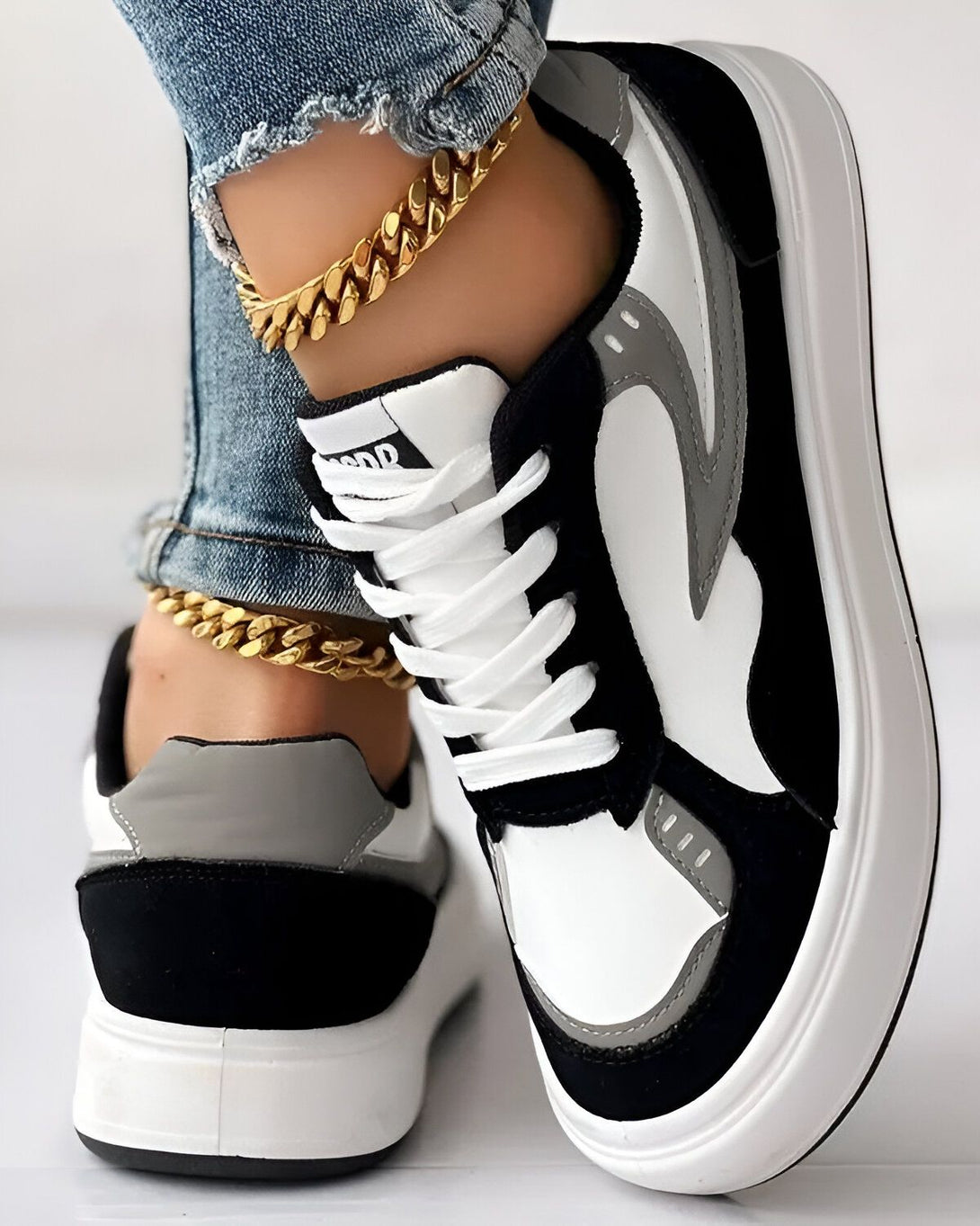 Une image d'une paire de baskets noires et blanches avec des lacets blancs. La basket est portée par une femme qui porte un jean bleu troué et une cheville dorée.