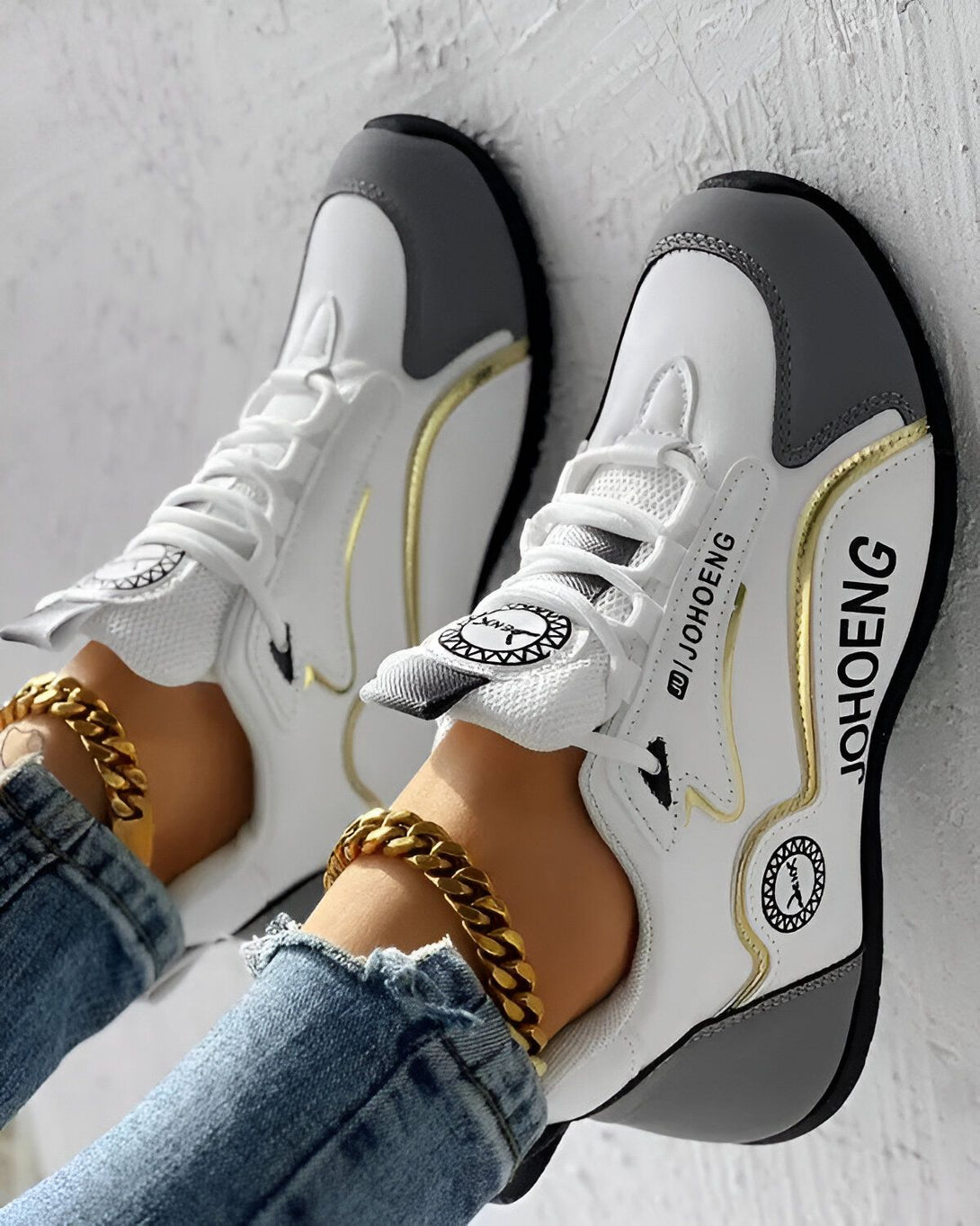 Une paire de baskets blanches et grises avec des lacets blancs et une semelle blanche. Le logo "JOHENG" est écrit en doré sur le côté de la basket.