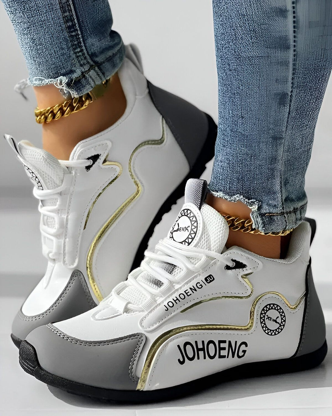 Une paire de baskets blanches et grises avec des lacets blancs et une semelle blanche. Le logo "JOHENG" est écrit en doré sur le côté de la basket.