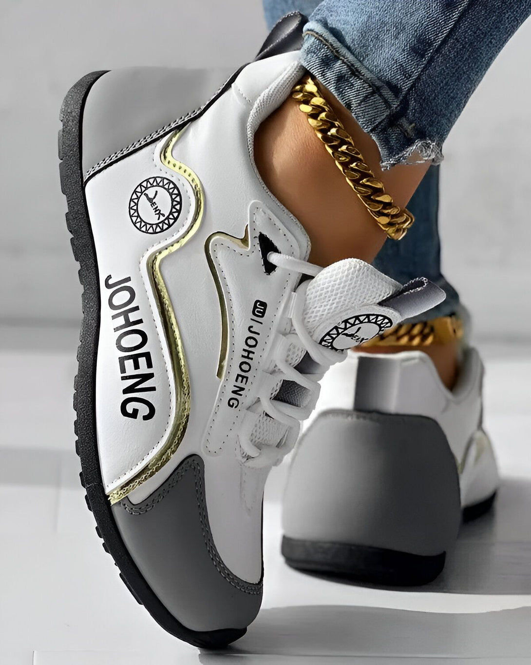 Une image d'une paire de baskets blanches et grises avec des lacets blancs et une semelle noire. Le logo "JOHOENG" est écrit sur le côté de la basket en lettres dorées.