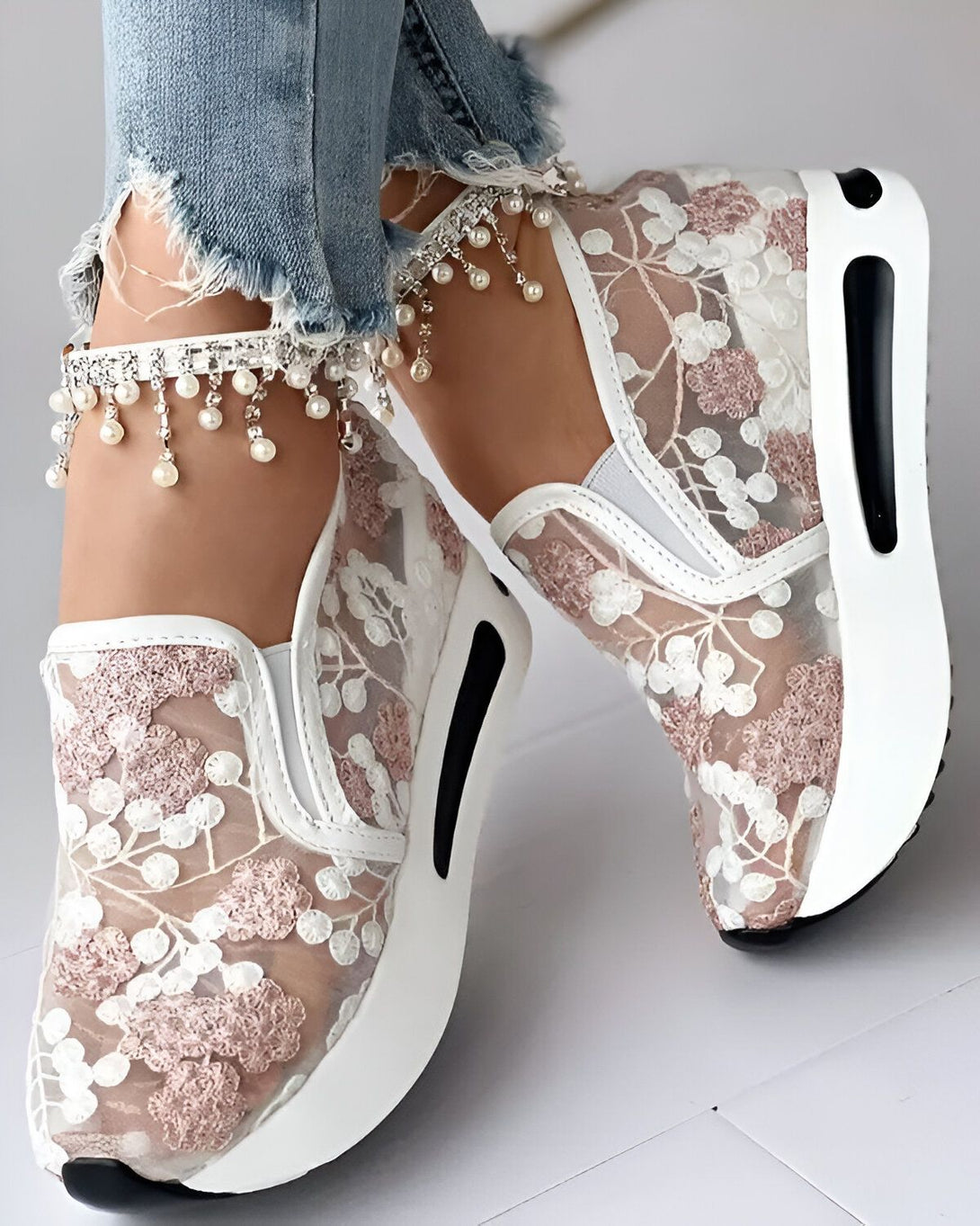 Une femme porte des baskets blanches avec des fleurs roses en dentelle. Les baskets ont une semelle compensée et sont très confortables.