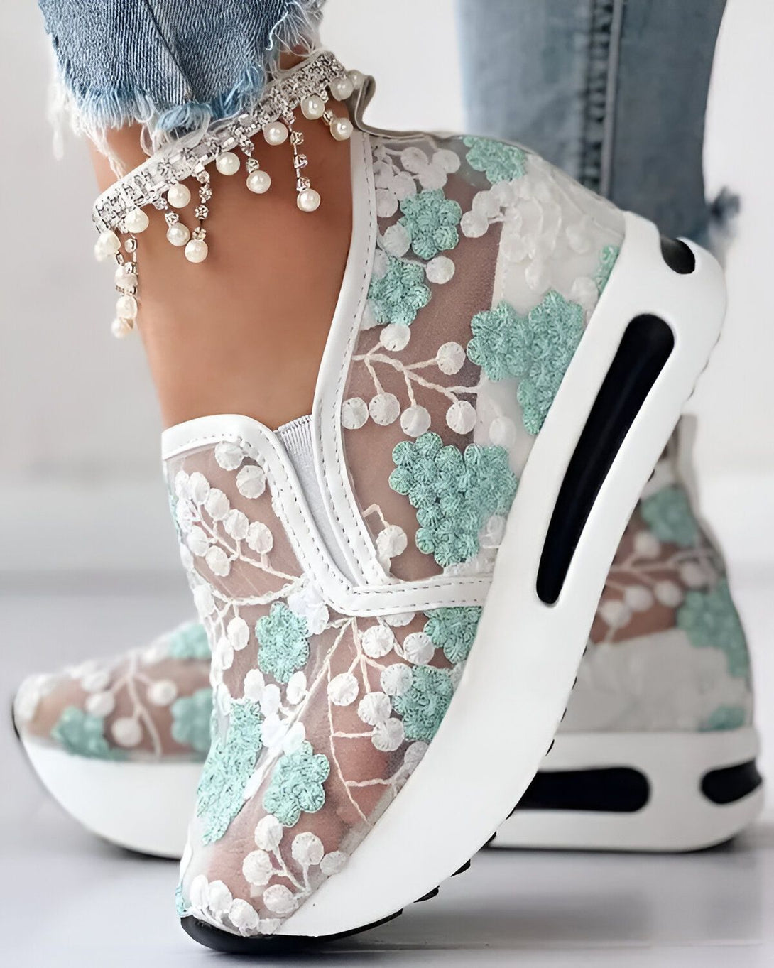 Une femme porte des baskets blanches en dentelle avec des fleurs vertes. Les baskets sont légères et semblent confortables. Elles sont parfaites pour le printemps et l'été.