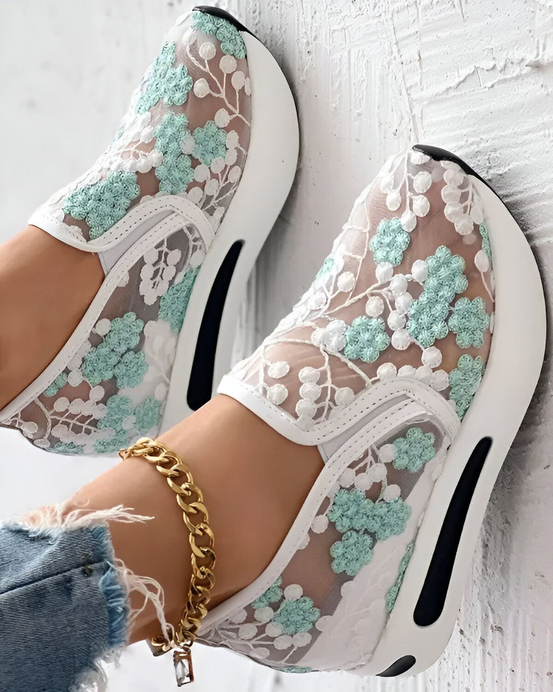 Une paire de baskets blanches avec des fleurs vertes en dentelle.