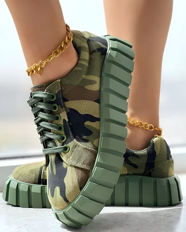 Une femme porte des baskets vertes et marrons à lacets avec une semelle épaisse. Elle porte également une chaîne dorée autour de la cheville.