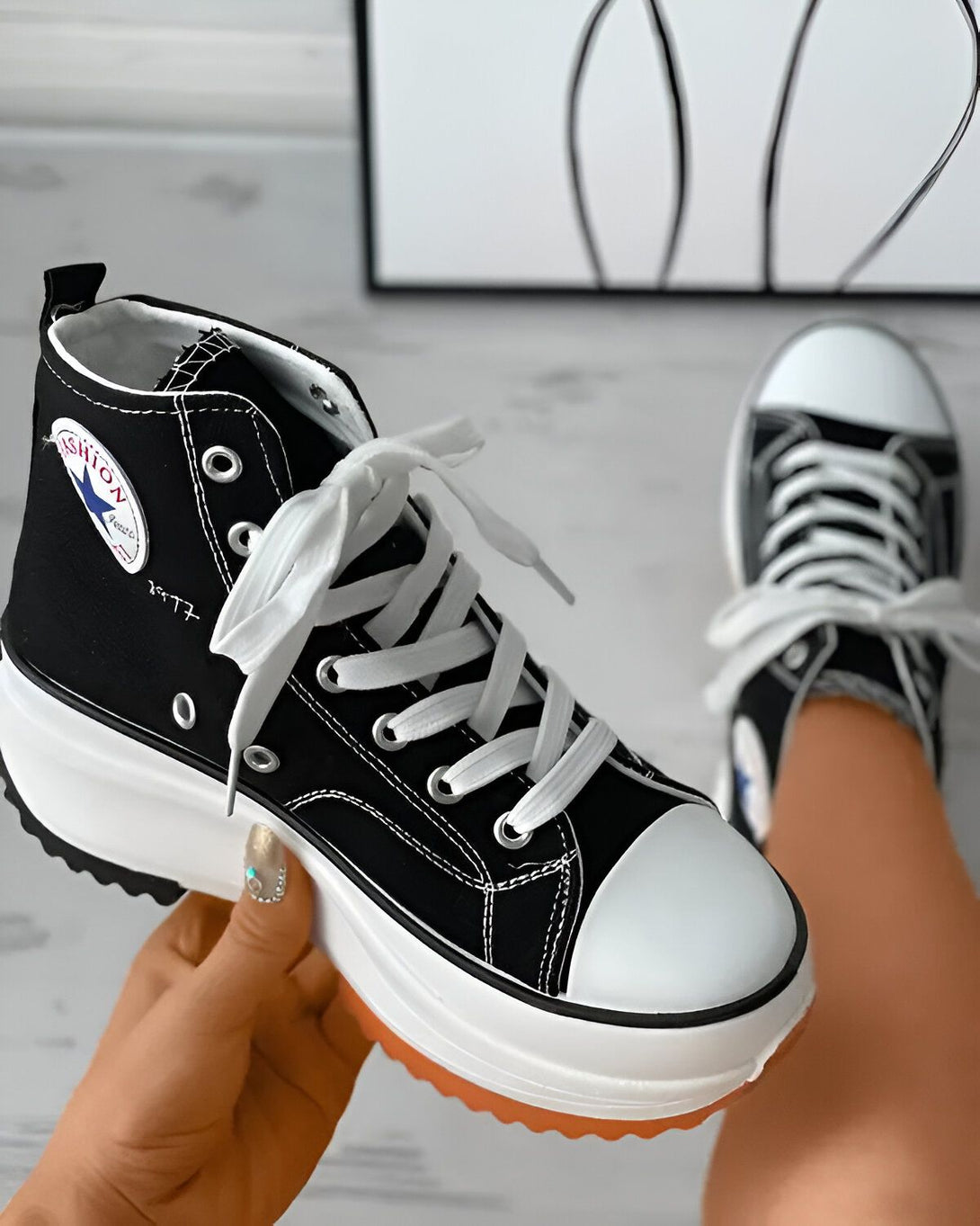Une image d'une paire de chaussures montantes noires et blanches avec des lacets blancs. Les chaussures sont portées par une femme et on peut voir sa main tenant la chaussure.