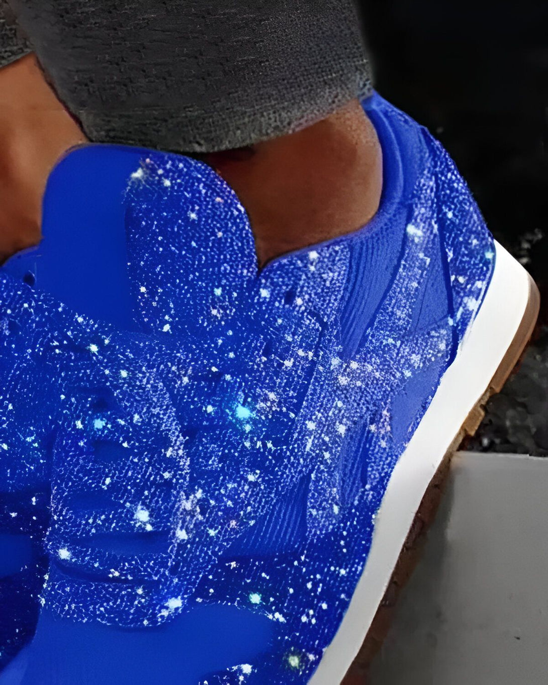 Une image d'une chaussure bleue avec des étoiles blanches. La chaussure est portée par une personne dont on ne voit que le pied et la cheville. Le sol est noir.