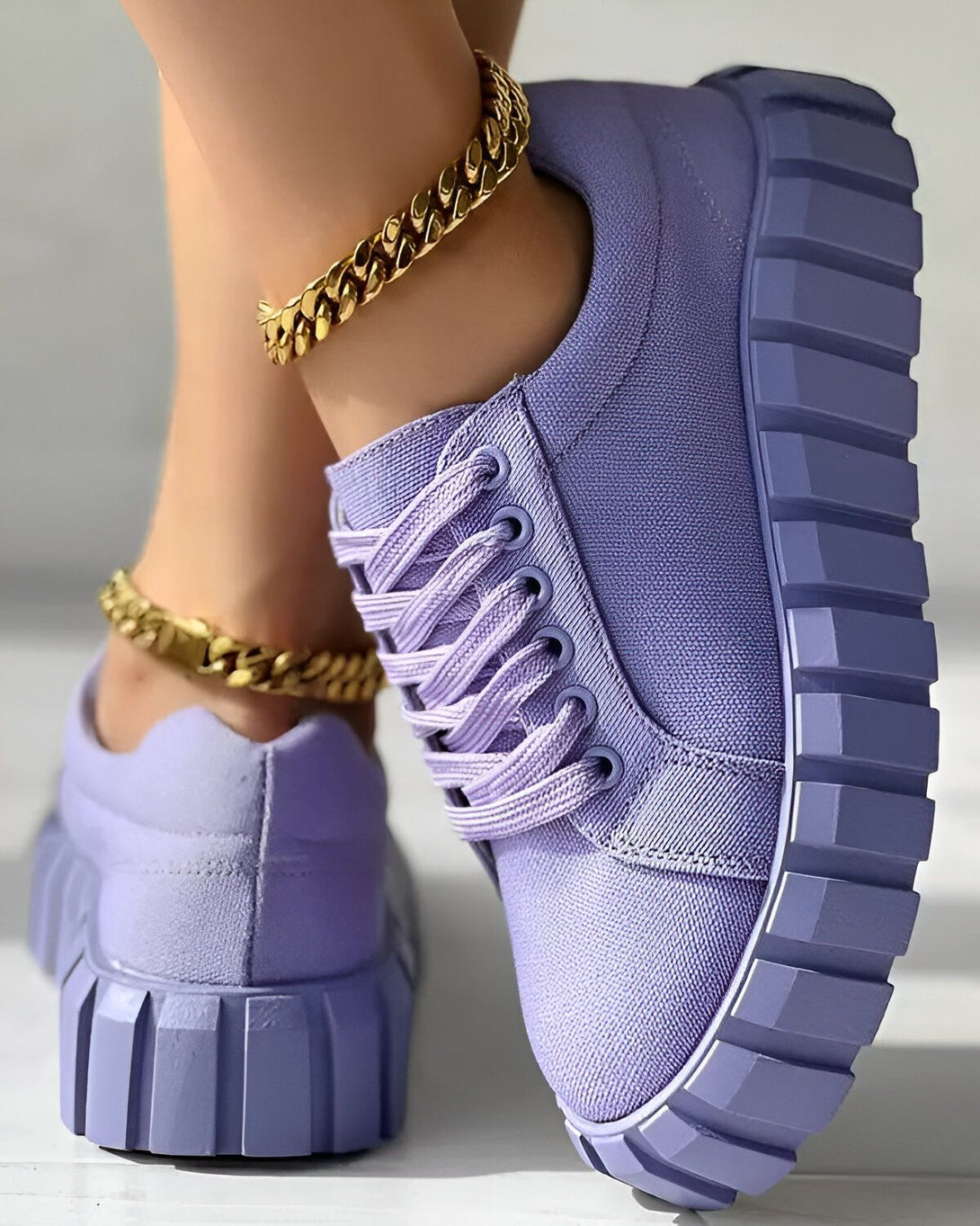 Une image d'une paire de chaussures violettes avec des lacets et une semelle épaisse. Les chaussures sont portées par une femme qui a une chaîne en or autour de la cheville.