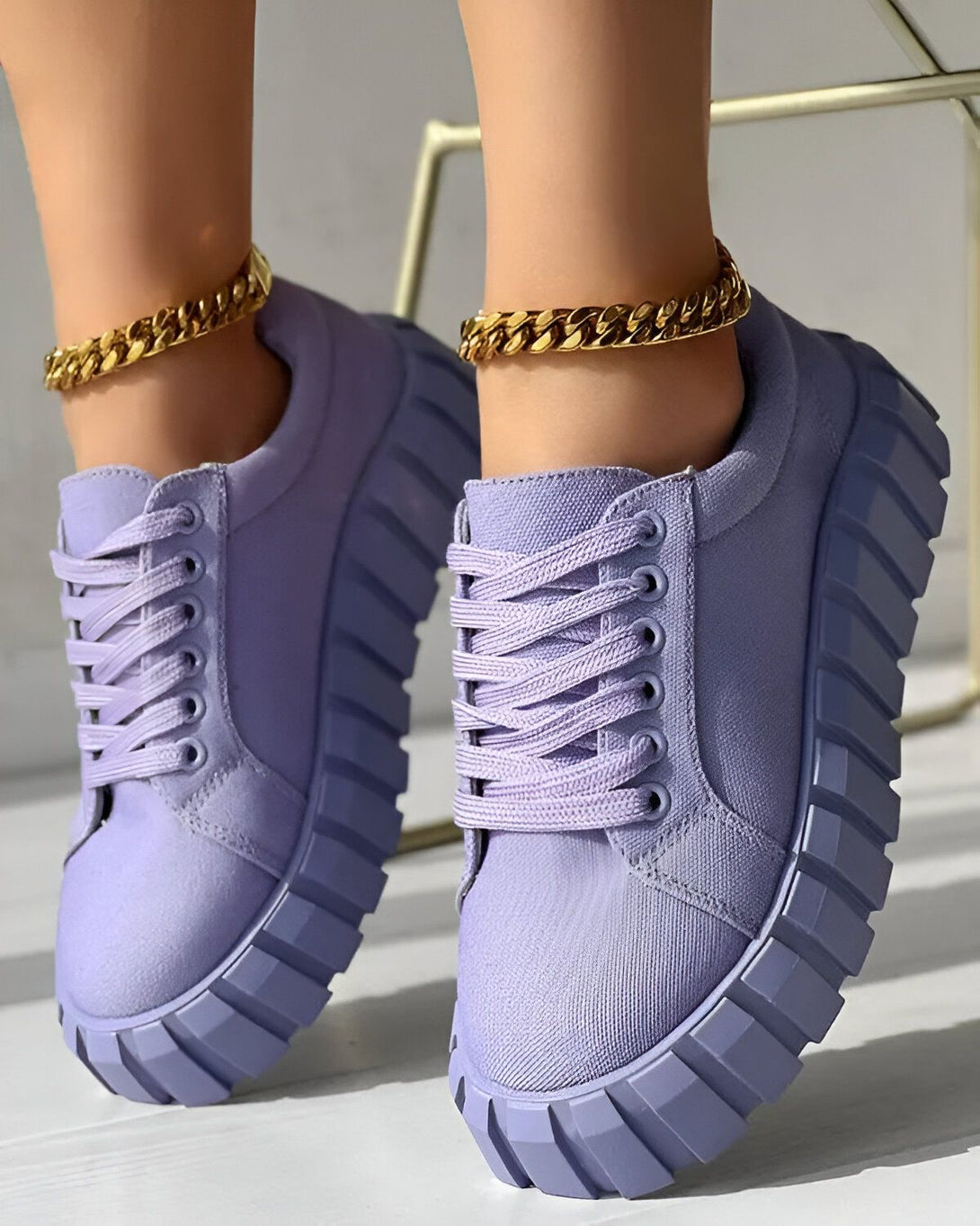 Une paire de baskets violettes avec des lacets et une semelle épaisse. Les baskets sont portées par une femme qui porte également un bracelet de cheville en or.