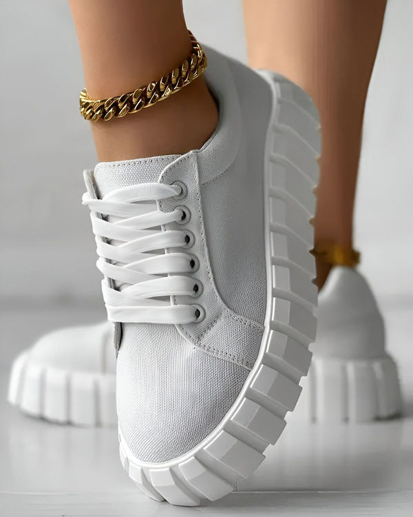 Une image d'une paire de baskets blanches avec des lacets blancs sur un pied avec une cheville avec un bracelet de cheville en or.