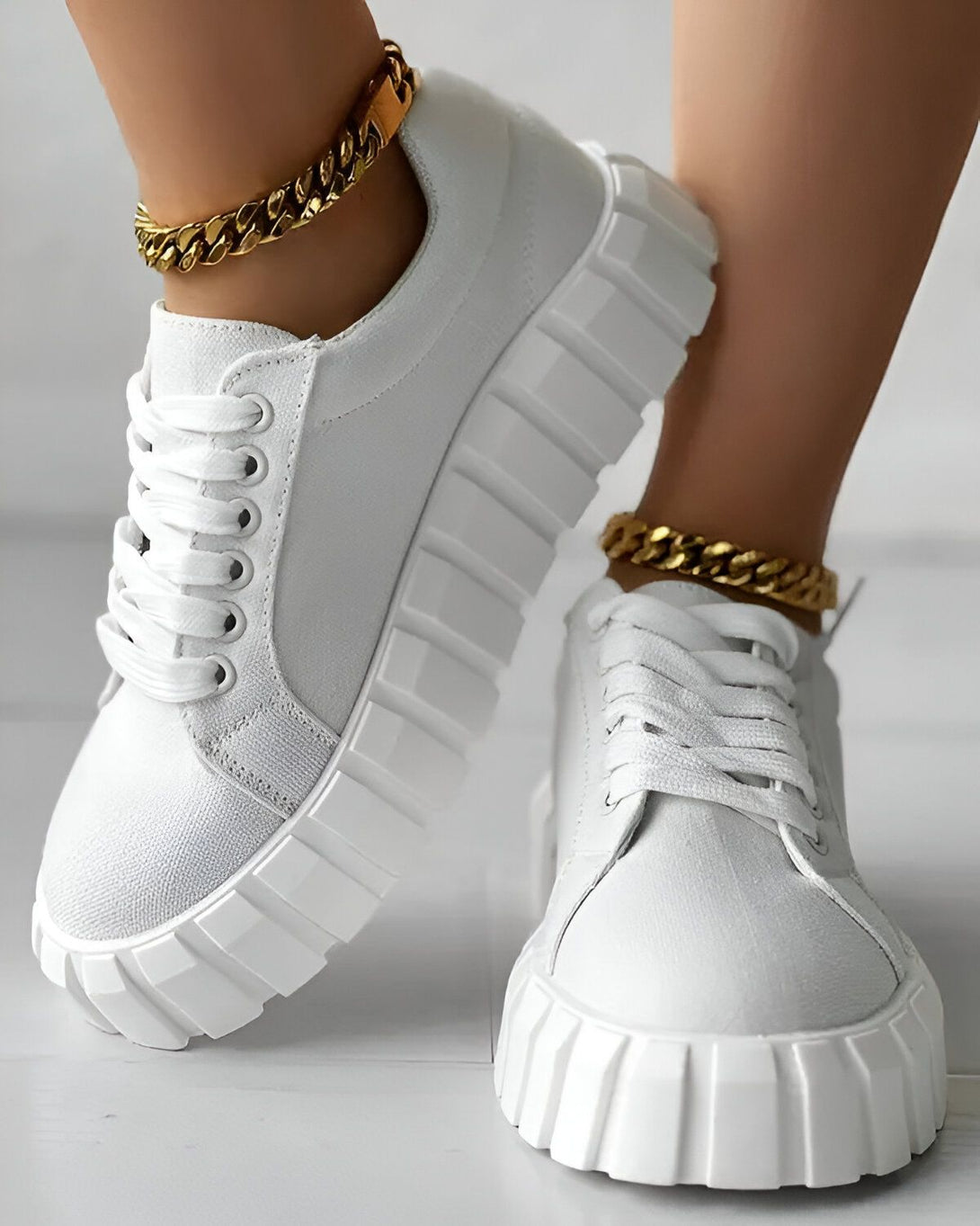 Une paire de baskets blanches avec des lacets blancs sur un sol en béton. Les baskets ont une semelle épaisse et crantée.