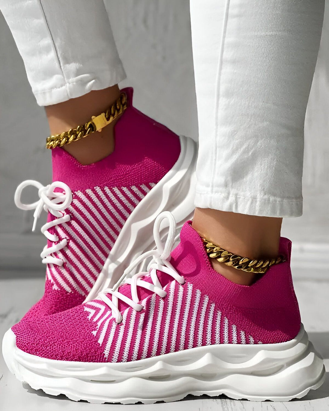 Une femme porte des baskets roses et blanches avec des lacets. Elle porte également un jean blanc et des chaussettes roses. Les baskets sont en maille et ont une semelle blanche.