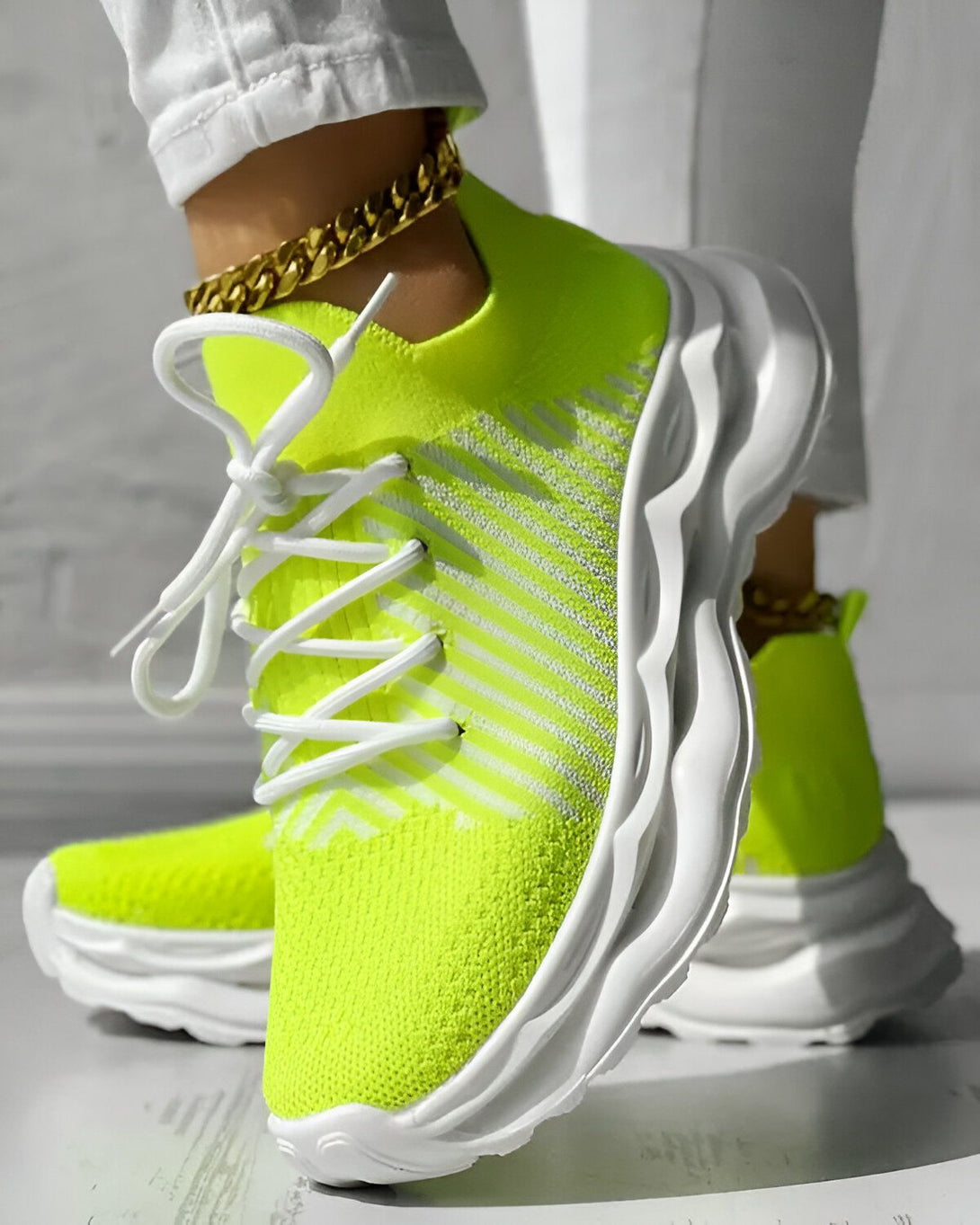 Une femme porte des baskets vert fluo avec des lacets blancs. Les baskets ont une semelle blanche et des rayures blanches sur le côté. La femme porte également un jean blanc et un haut blanc.