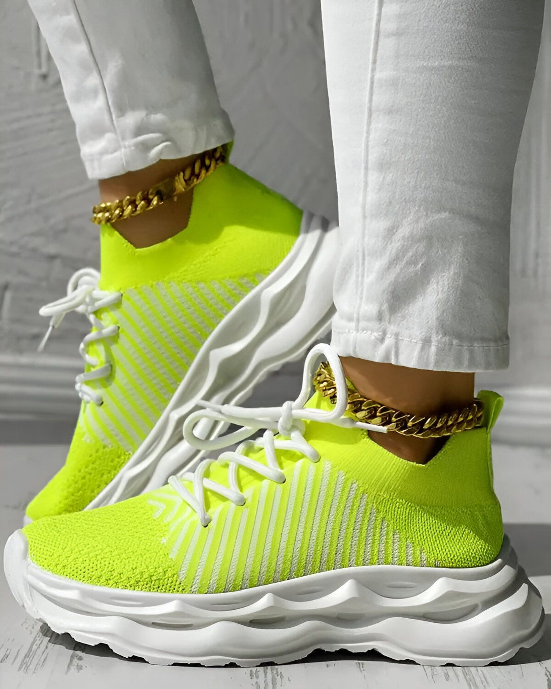 Une femme porte des baskets vert fluo avec des lacets blancs et des semelles blanches. Elle porte également un jean blanc et des chaussettes blanches.