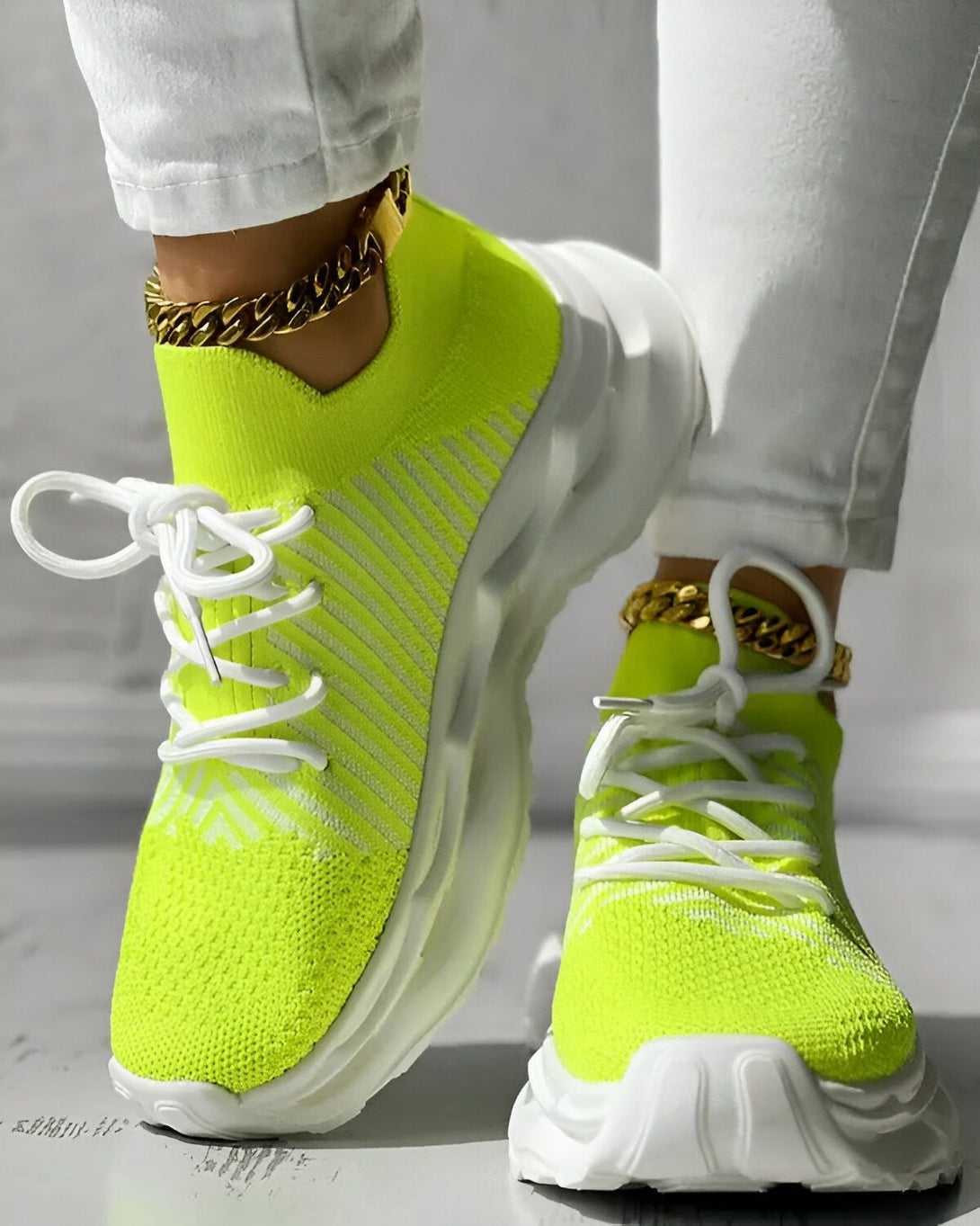 Une femme porte des baskets vert fluo avec des lacets blancs. Elle porte également un pantalon blanc et des chaussettes blanches. Les baskets sont en maille et ont une semelle blanche.