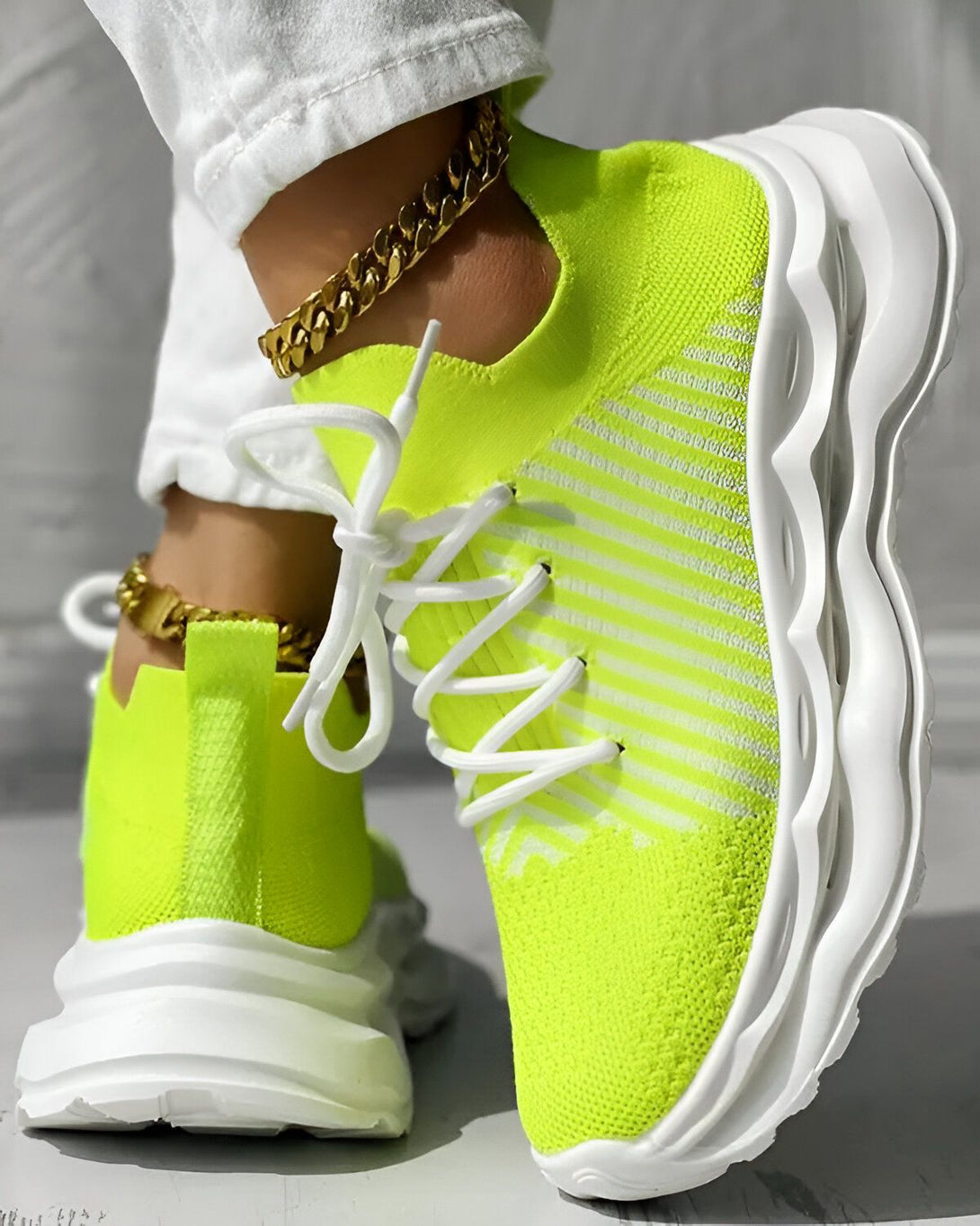 Une femme porte des baskets vert fluo avec des lacets blancs. Elle porte également un jean blanc et des chaussettes blanches. Les baskets sont de la marque Nike et ont une semelle blanche.