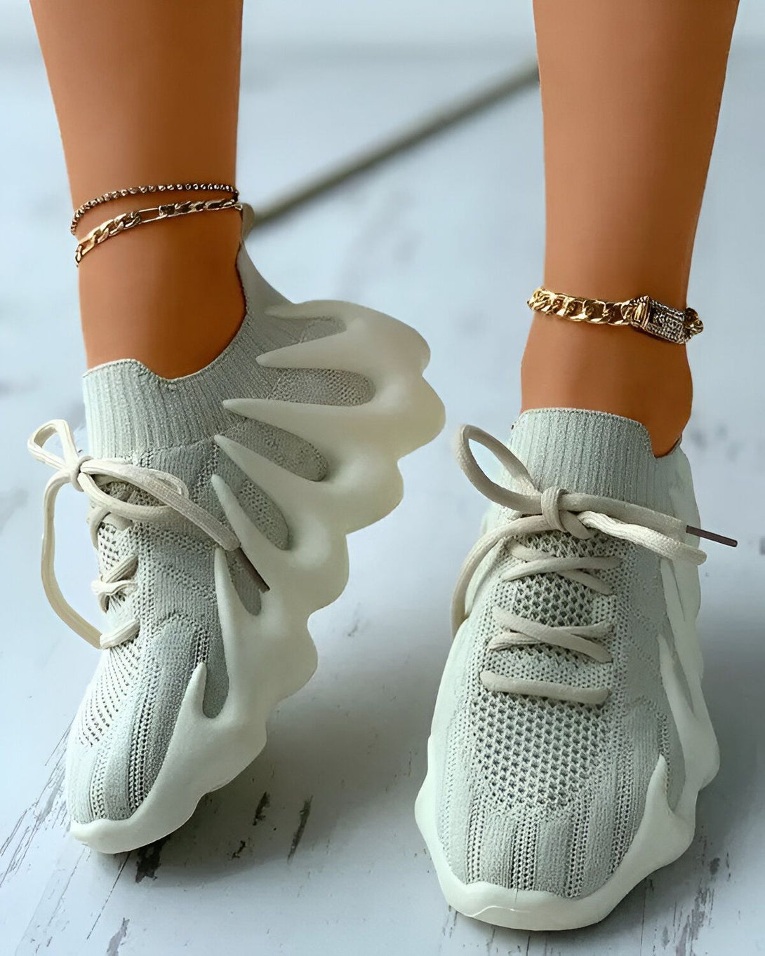 Une paire de baskets grises à lacets avec une semelle épaisse et crantée. Les baskets sont portées par une femme qui porte également un jean et un t-shirt.