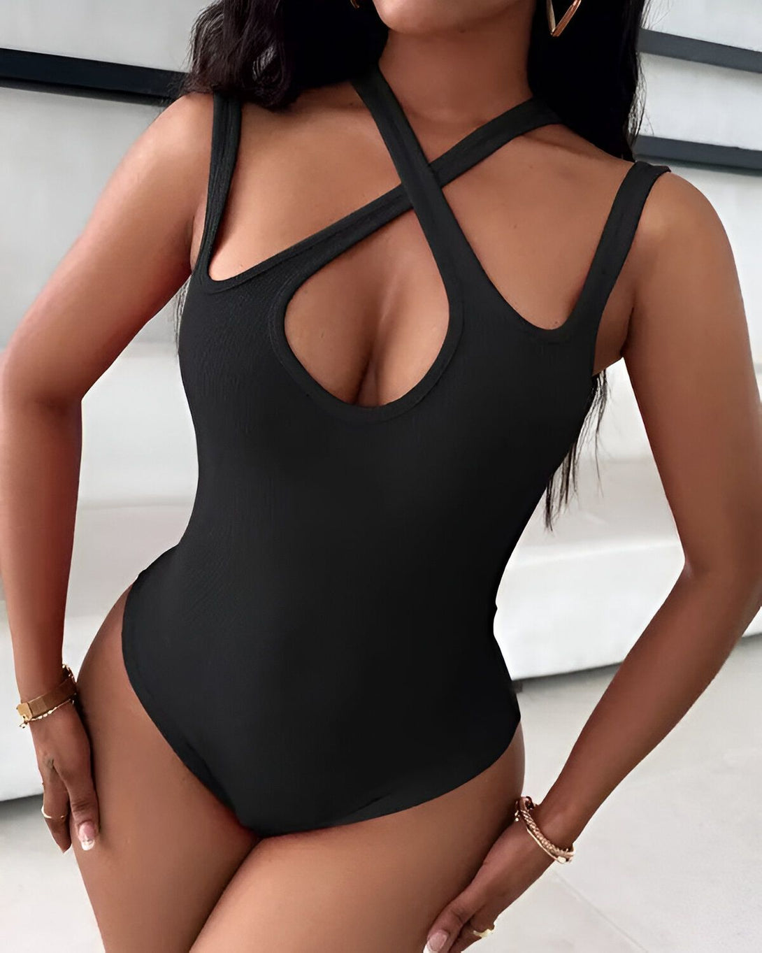 Une femme porte un body noir avec des bretelles croisées sur le devant. Le body est échancré sur les côtés et a une encolure dégagée.
