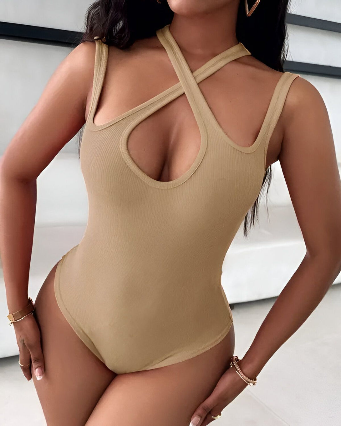 Une femme porte un body beige avec des bretelles croisées sur le devant. Le body est échancré sur les côtés et au niveau de la poitrine.