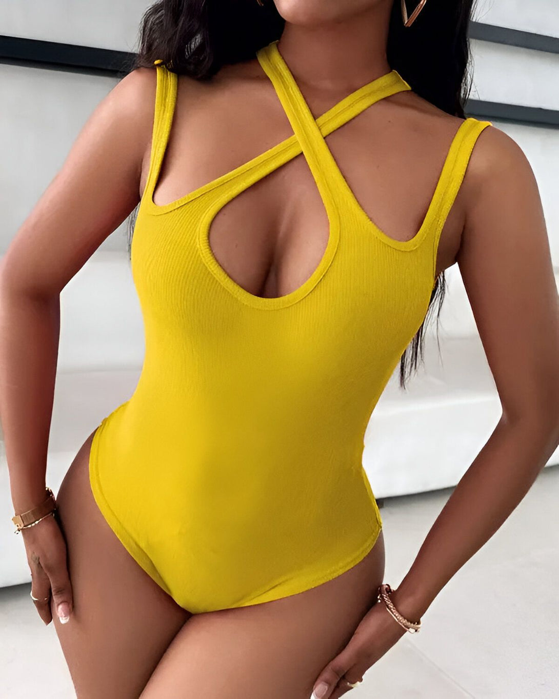 Une femme porte un body jaune avec des bretelles croisées sur le devant. Le body est échancré sur les côtés et a une encolure plongeante.