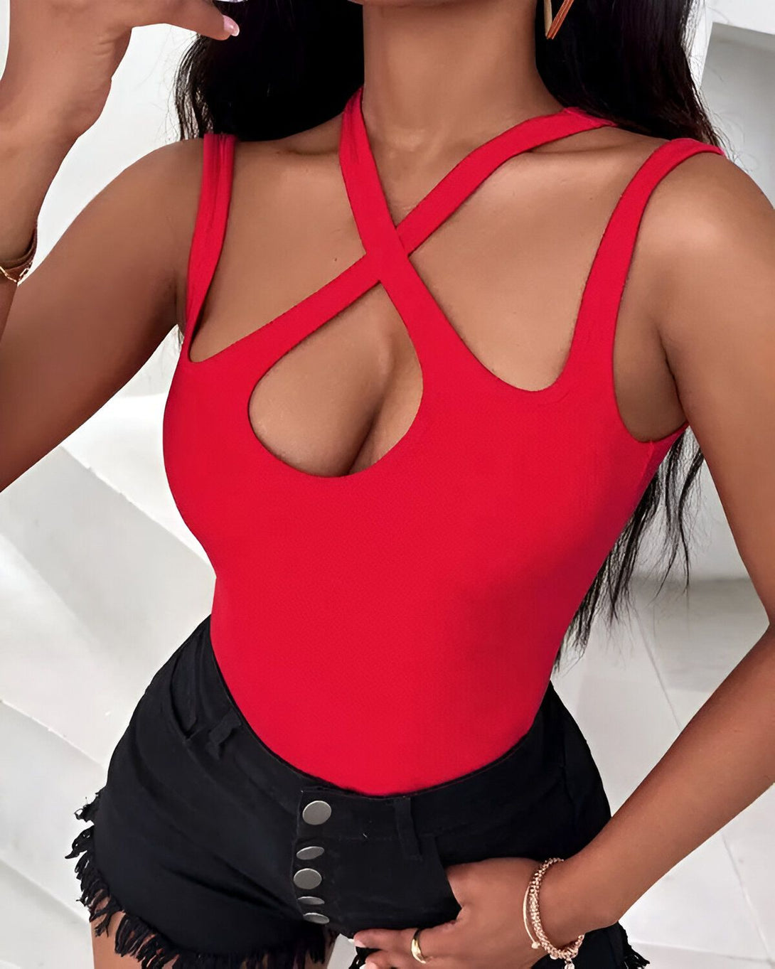 Une femme porte un body rouge moulant avec un décolleté croisé. Elle porte également un short en jean noir taille haute.