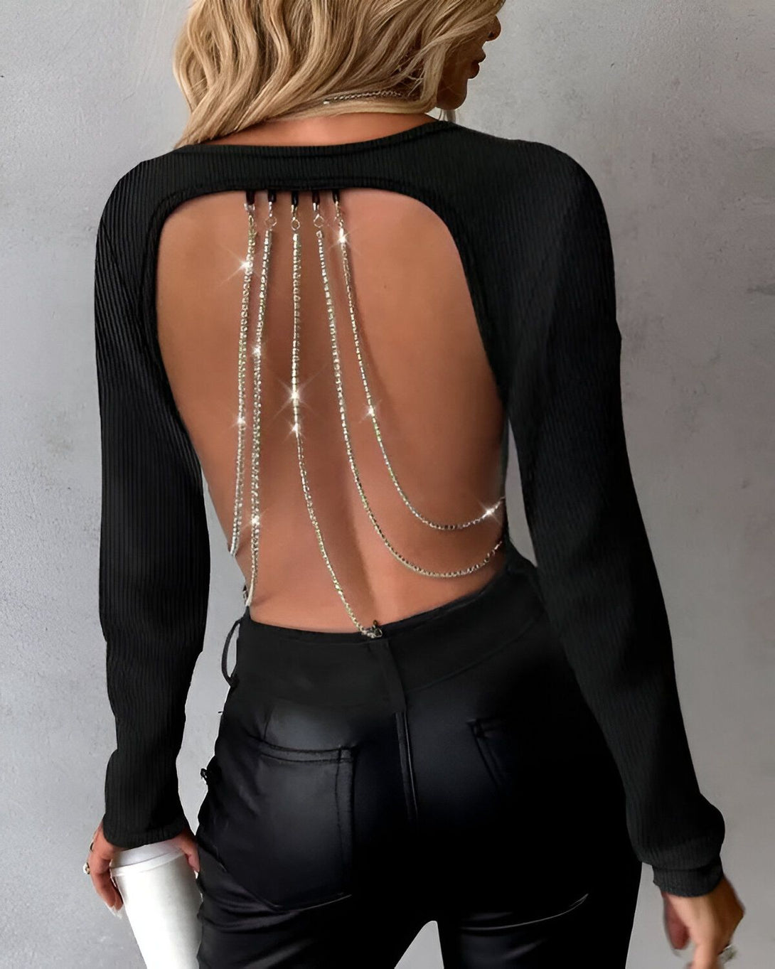 Une femme porte un haut noir à manches longues avec un dos ouvert et des chaînes en strass.