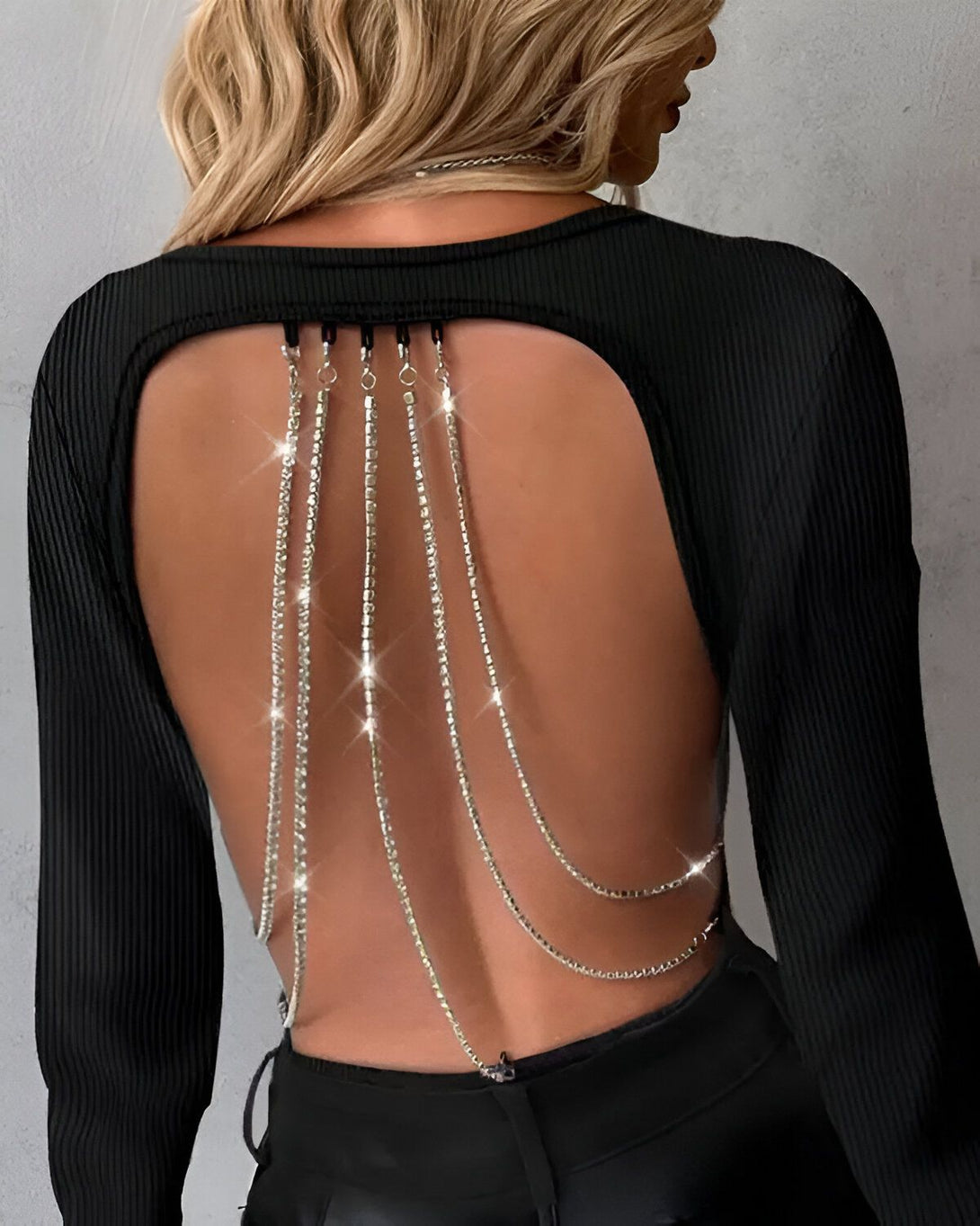 Une femme porte un haut noir avec un dos ouvert et des chaînes en strass qui pendent.