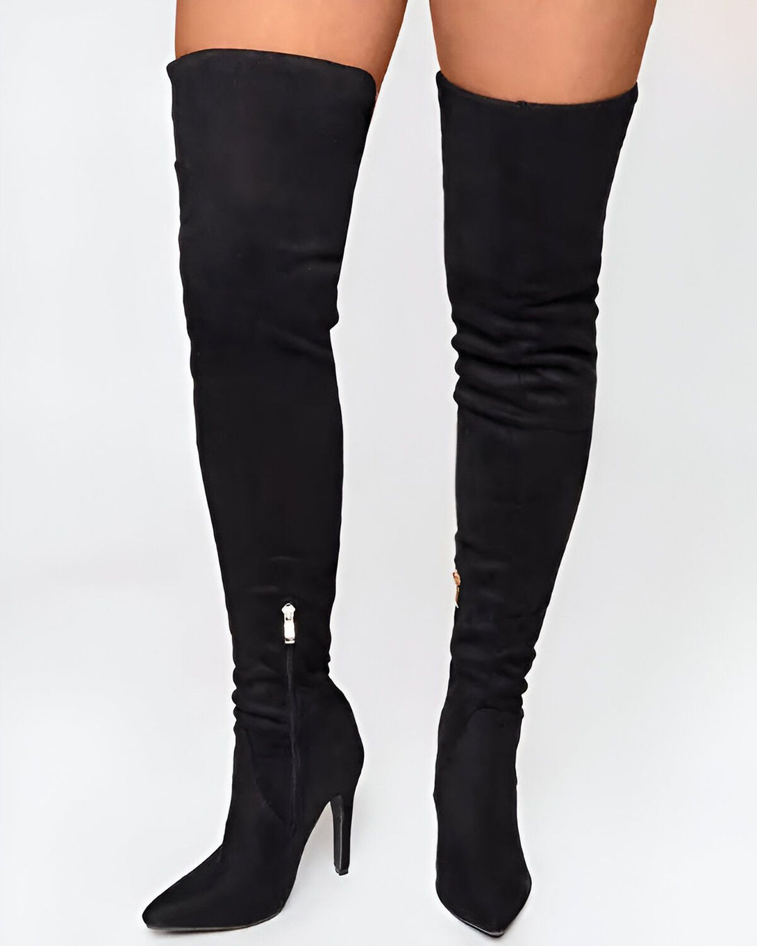 Une femme porte des bottes noires à talons hauts. Les bottes sont en daim et montent jusqu'au-dessus du genou. La femme est debout, les jambes légèrement écartées. On ne voit que ses jambes et ses pieds.