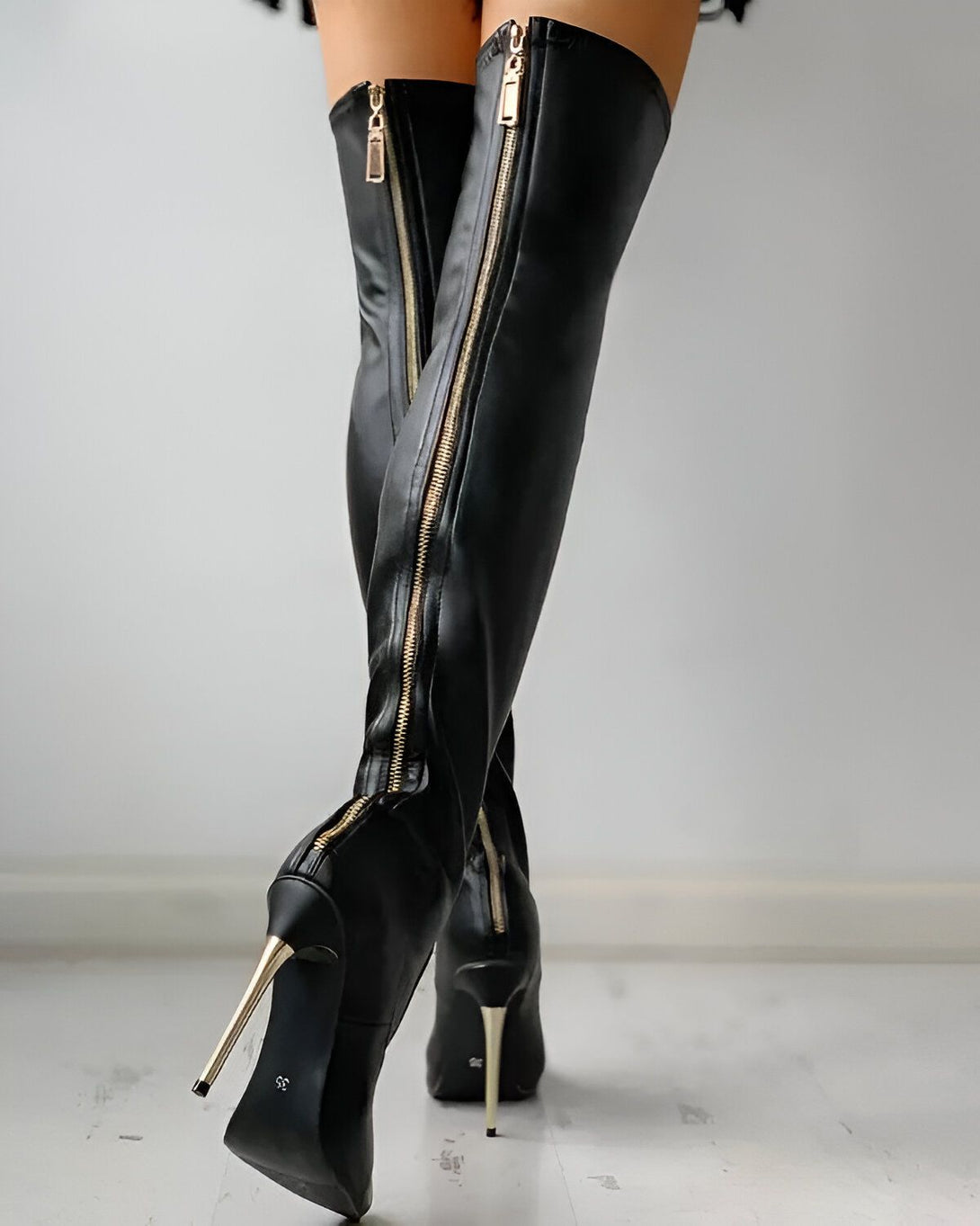 Une femme porte des bottes noires à talons hauts. Les bottes sont en cuir et ont une fermeture éclair dorée à l'arrière. La femme est debout, dos à la caméra.