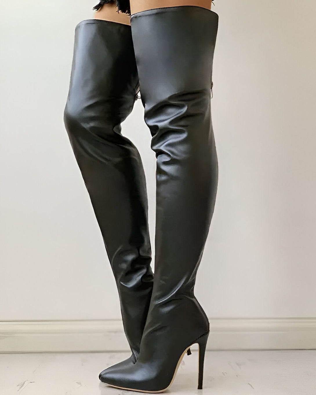 Une femme porte des bottes noires à talons hauts. Les bottes sont en cuir et montent jusqu'à la cuisse. La femme est debout, face à l'appareil photo.