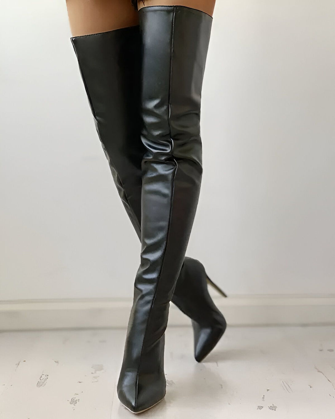 Une femme porte des bottes noires à talons hauts. Les bottes sont en cuir et montent jusqu'à la cuisse. La femme est debout, face à l'appareil photo. On ne voit que ses jambes et ses pieds.