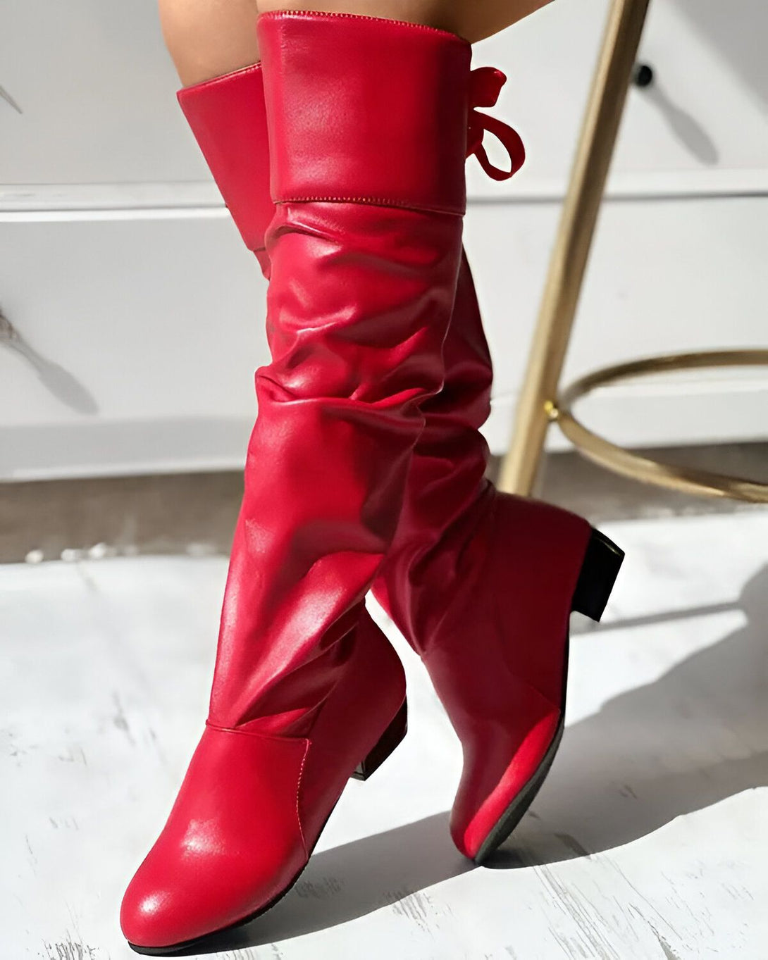 Une femme porte des bottes rouges à talons hauts. Les bottes sont en cuir et ont un bout pointu. La femme est debout sur un sol en marbre.