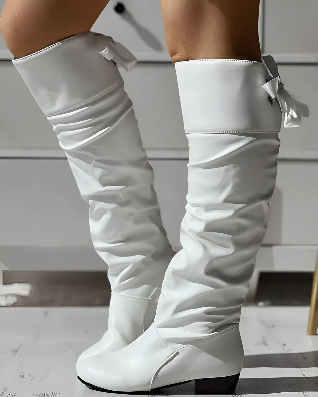 Une femme porte des bottes blanches à talons hauts. Les bottes sont en cuir et ont un nœud à l'arrière.