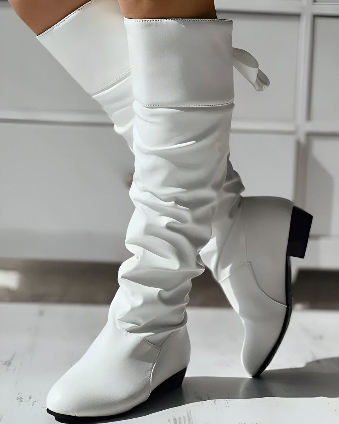 Une femme porte des bottes blanches à talons hauts. Les bottes sont en cuir et ont une tige froncée.