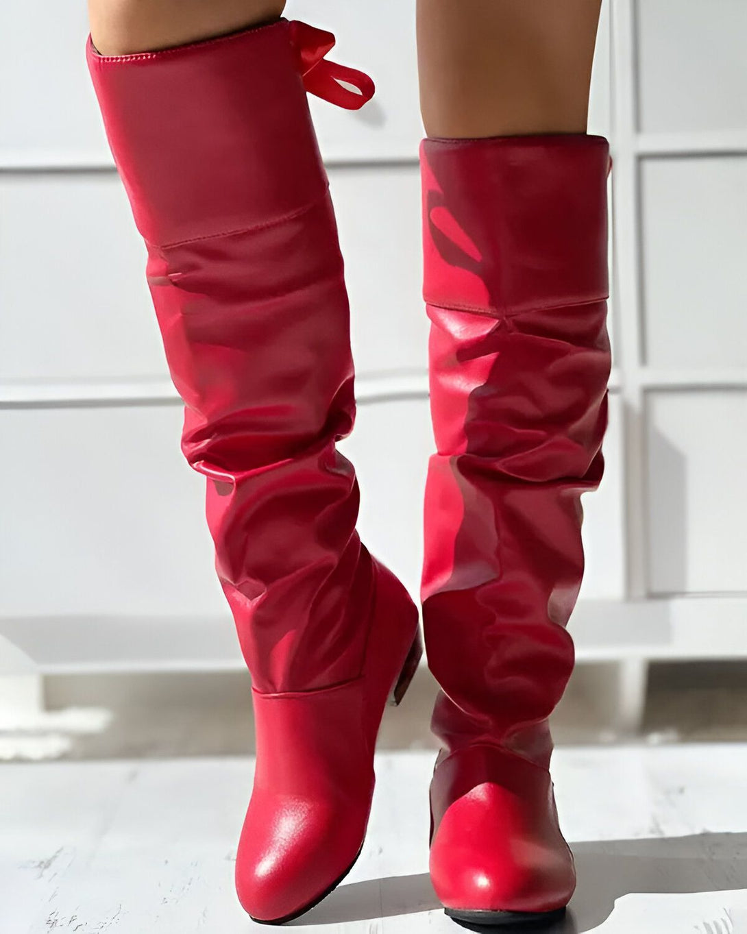Une femme porte des bottes rouges à talons hauts. Les bottes sont en cuir et ont un bout pointu. La femme est debout sur un sol en marbre blanc.