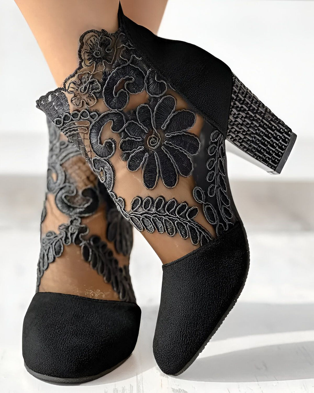 Une paire de bottines noires à talons hauts avec des motifs floraux en dentelle.