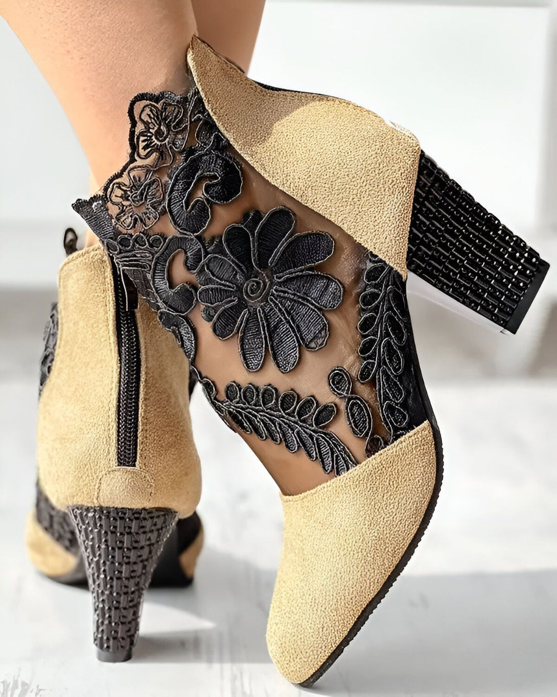 Une paire de bottines beiges à talons hauts avec des fleurs en dentelle noire sur le côté.