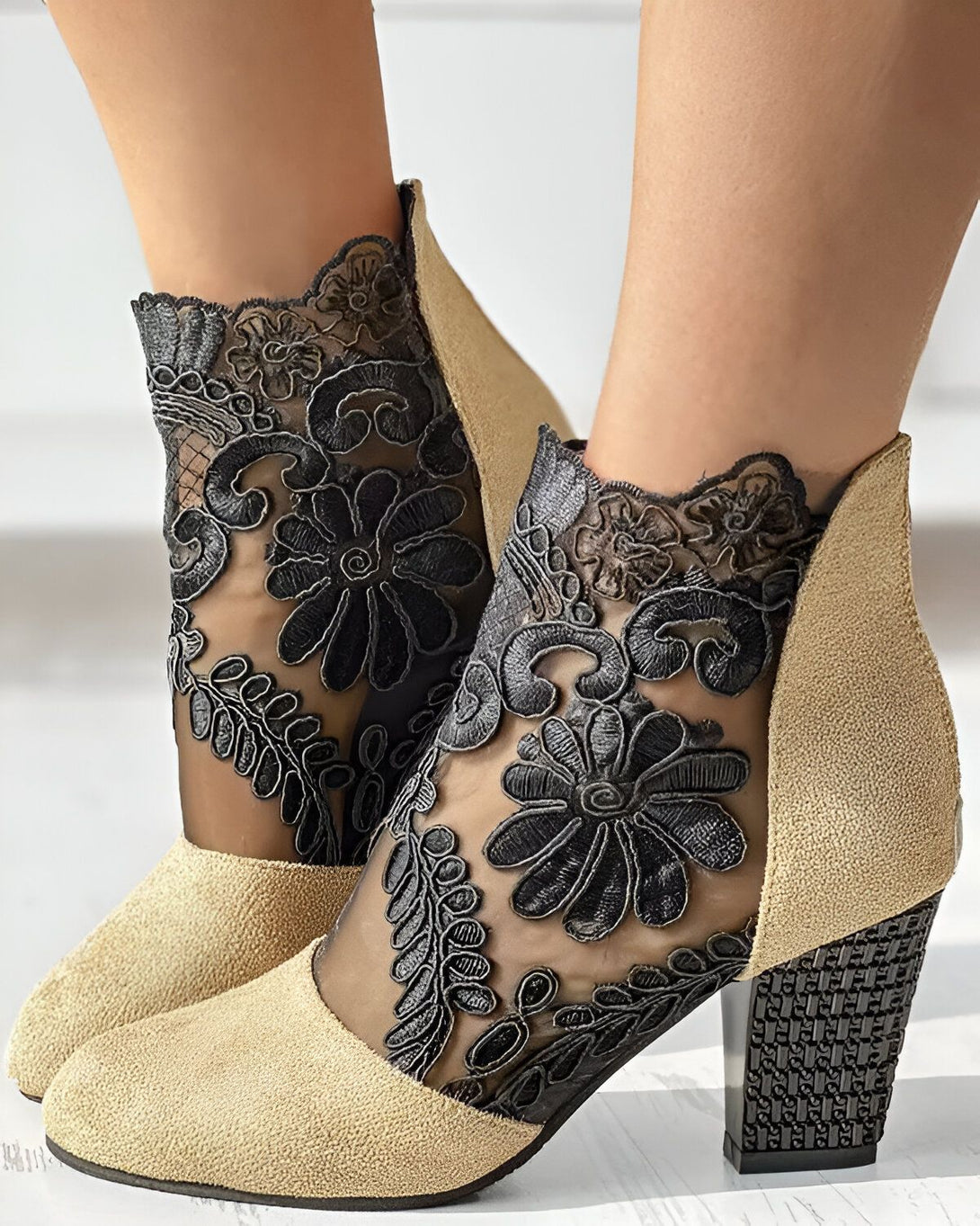 Une paire de bottines beige à talons hauts avec un empiècement en dentelle noire sur le dessus.
