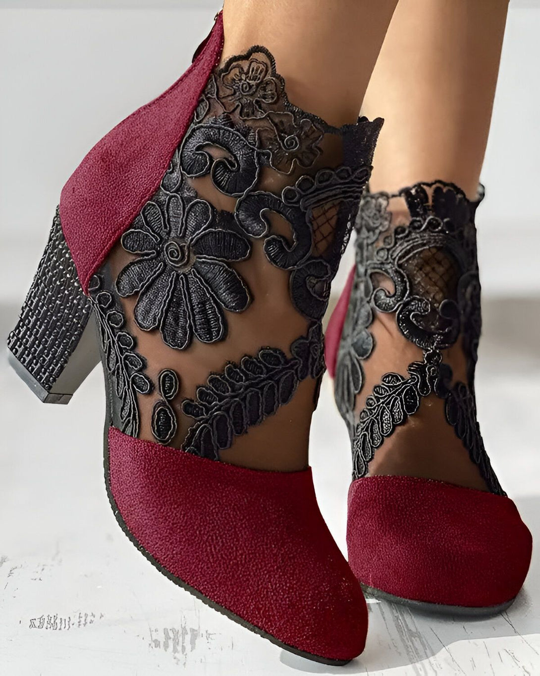 Une paire de bottines rouges à talons hauts avec des motifs floraux noirs en dentelle.