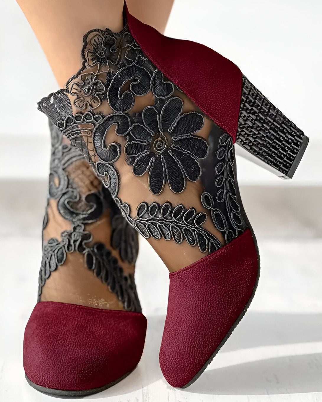 Une paire de bottines rouges à talons hauts avec des motifs floraux noirs en dentelle.