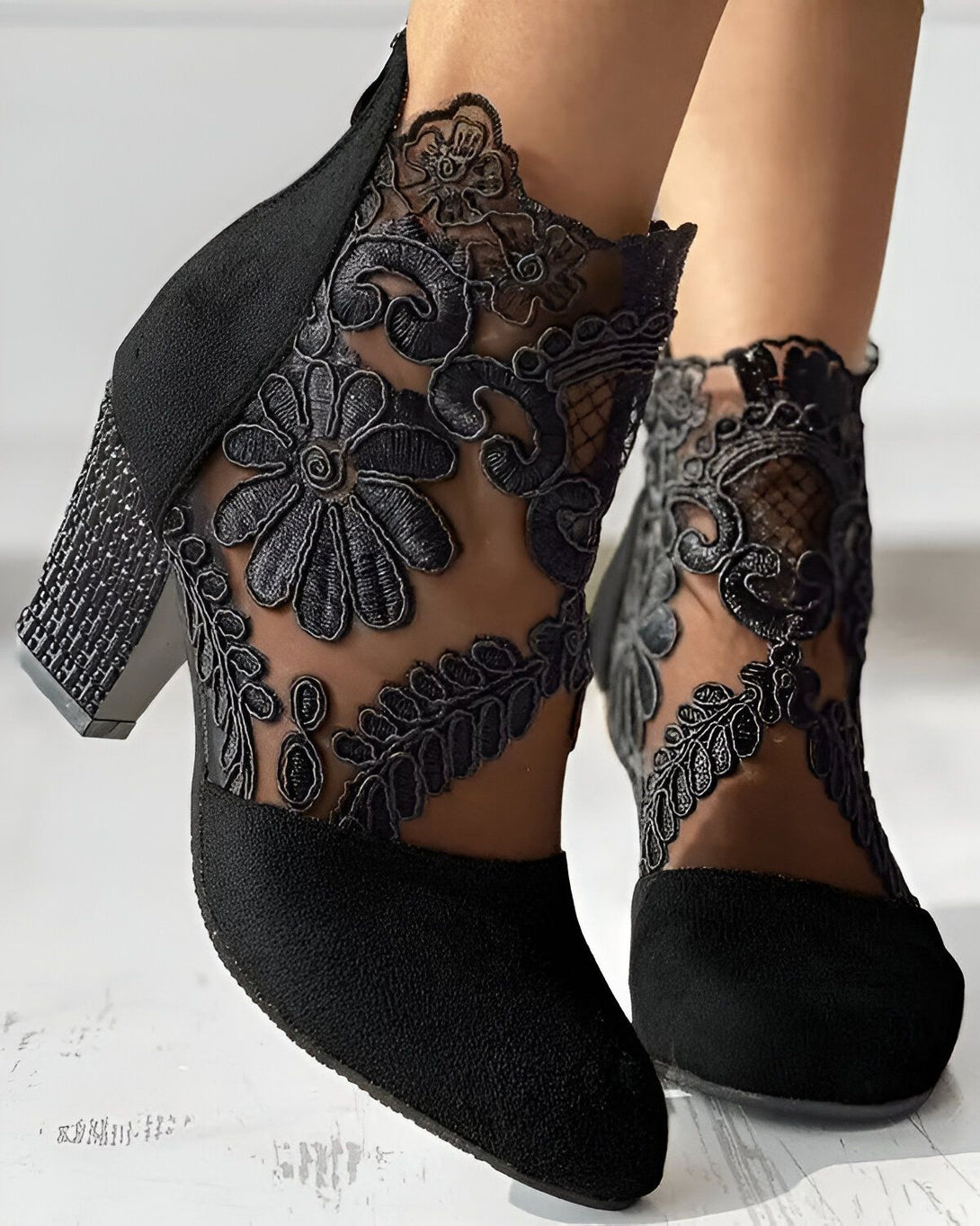 Une paire de bottines noires à talons hauts avec des motifs floraux en dentelle.