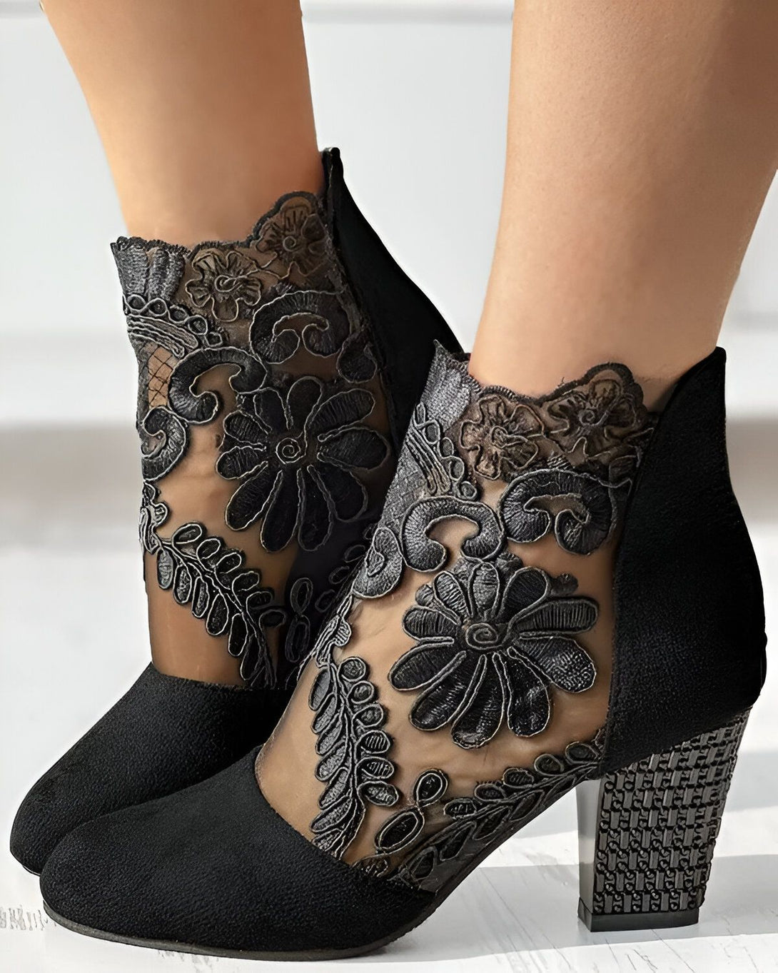 Une paire de bottines noires à talons hauts avec des motifs floraux en dentelle.