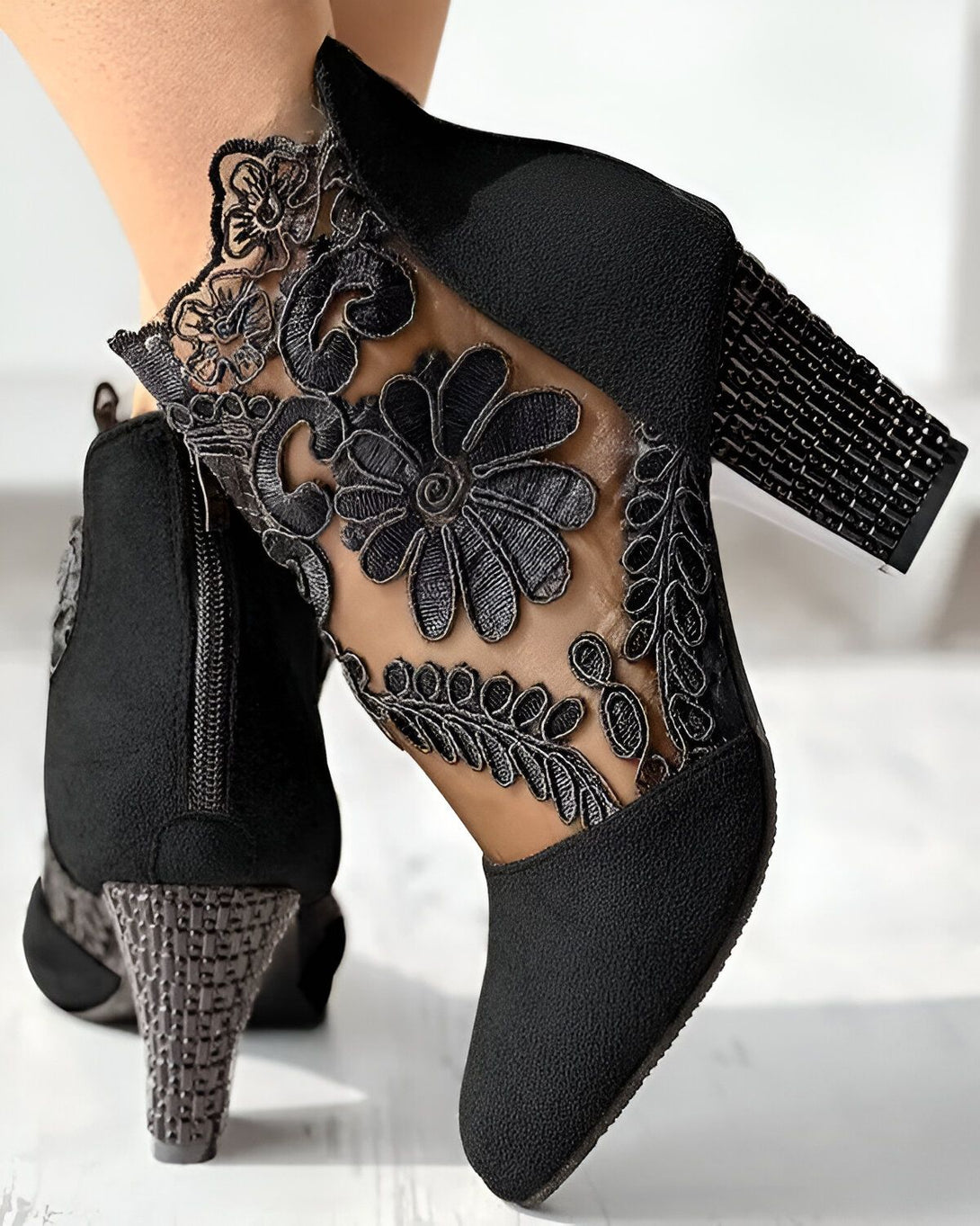 Une paire de bottines noires à talons hauts avec des fleurs en dentelle sur le côté.