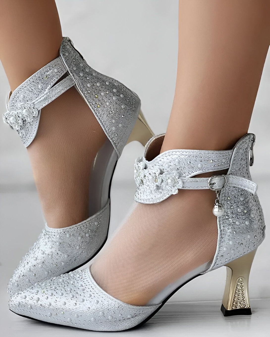 Une paire d'escarpins argentés à talons hauts. Les escarpins sont ornés de perles et de fleurs en strass.