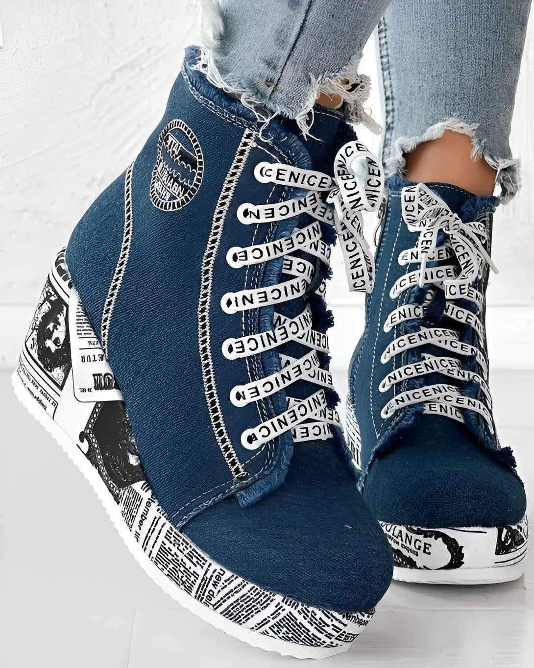 Une paire de bottines compensées en jean bleu avec des lacets blancs. Les semelles compensées sont blanches avec des motifs de journaux.