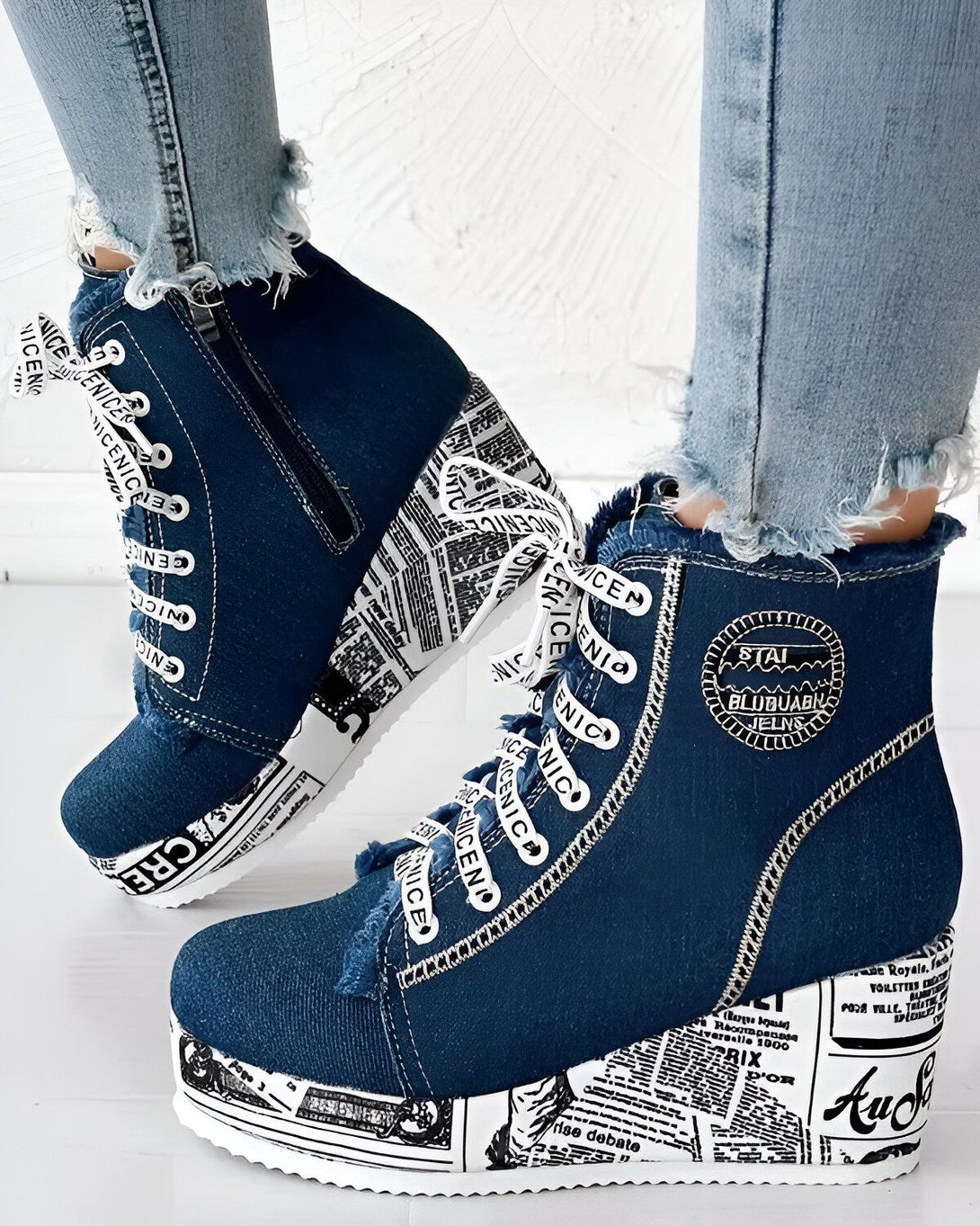 Une paire de chaussures compensées en jean bleu avec des lacets blancs et une semelle blanche. Les chaussures sont décorées de motifs de journaux.