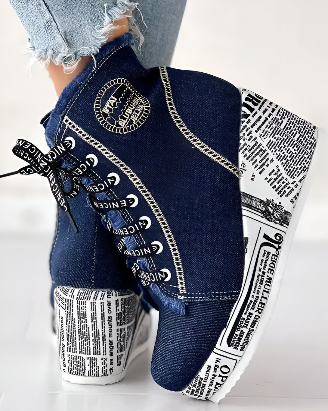 Une paire de bottes à talons compensés en jean bleu avec des lacets noirs. Les bottes sont décorées de surpiqûres blanches et d'un imprimé journal.