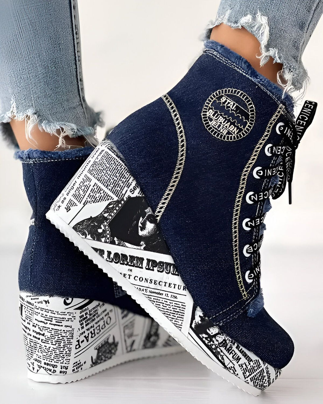 Une paire de bottines compensées en jean bleu avec des lacets et une semelle compensée blanche. Les bottines sont décorées de texte noir et blanc.
