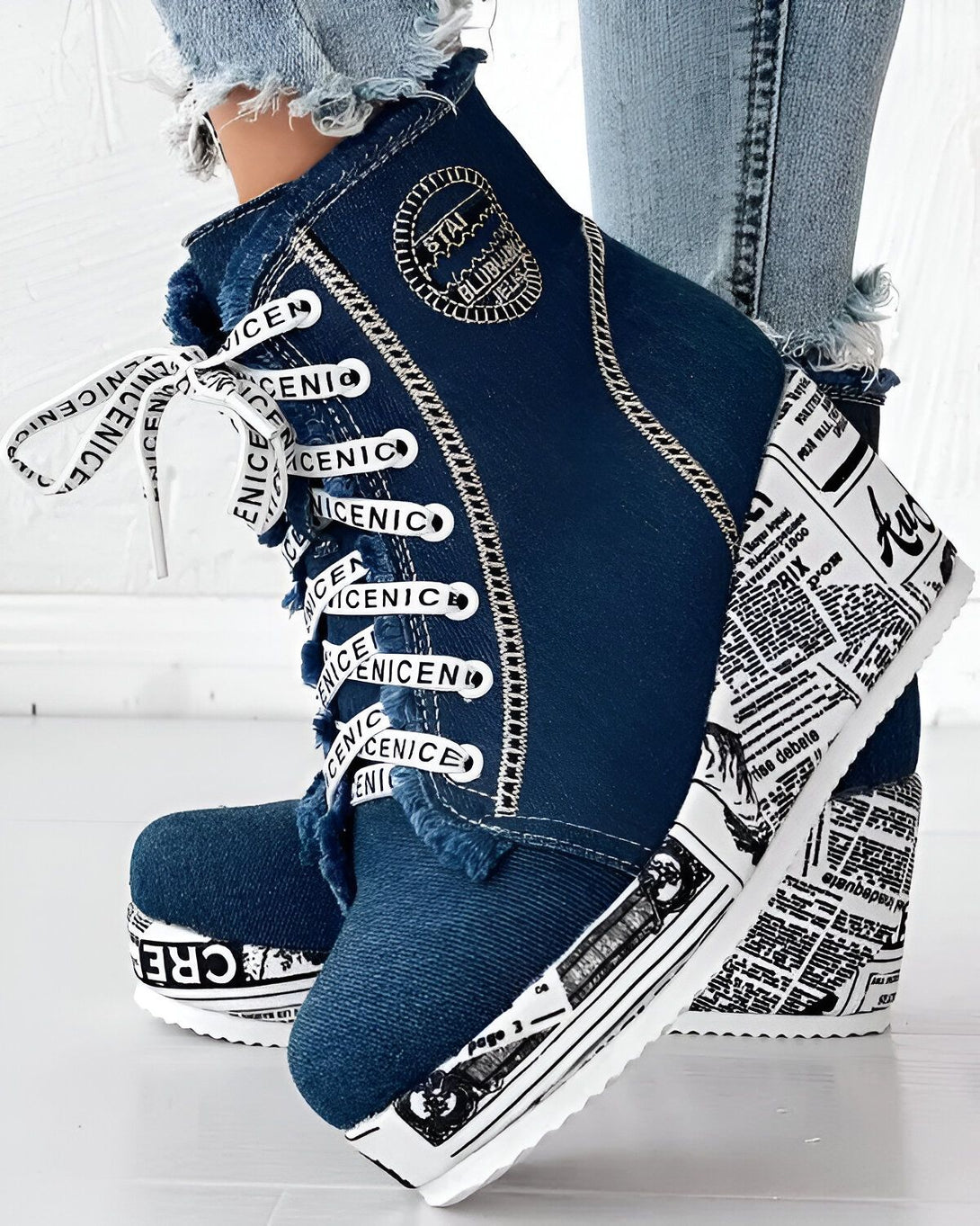 Une paire de bottes compensées en jean bleu avec des lacets blancs et une semelle blanche. Les bottes sont ornées d'un imprimé journal.
