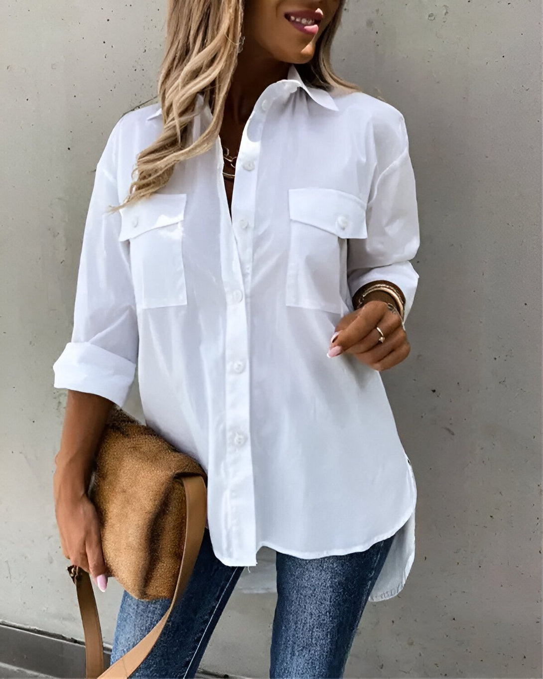 Une jeune femme porte une chemise blanche oversize avec un jean bleu et un sac à main marron.
